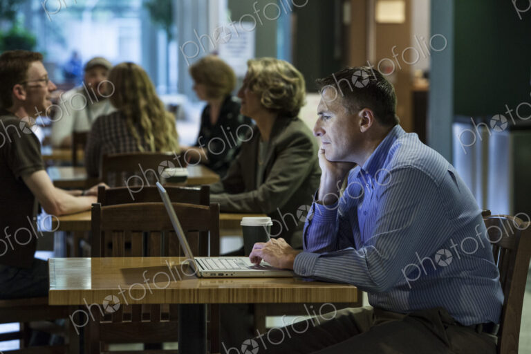 A caucasian businessman working on a laptop computer while sitting in a cafe.