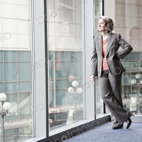 A caucasian businesswoman standing next to a large window in a convention center lobby.