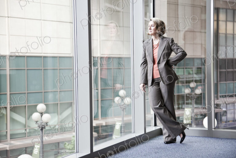 A caucasian businesswoman standing next to a large window in a convention center lobby.