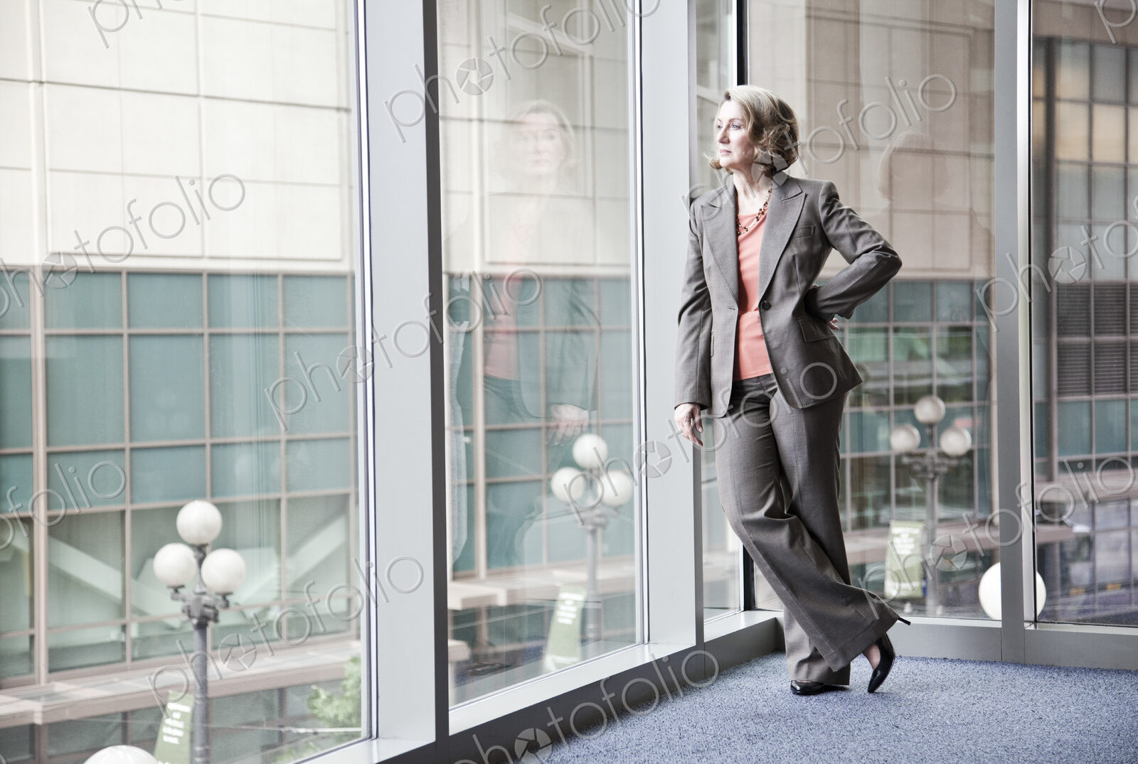 A caucasian businesswoman standing next to a large window in a convention center lobby.