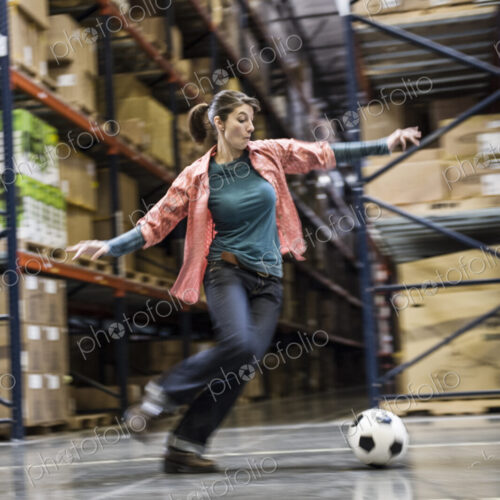 A caucasian female aboiut to kick a soccer ball during a work break in a distribution… A caucasian female aboiut to kick a soccer ball during a work break in a distribution…