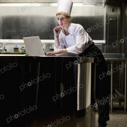 A caucasian female chef working on a laptop computer after hours in a commercial kitchen. A caucasian female chef working on a laptop computer after hours in a commercial kitchen.