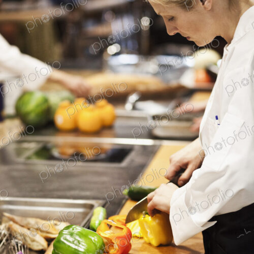A caucasian female chef works cutting vegetables in a commercial kitchen, A caucasian female chef works cutting vegetables in a commercial kitchen,