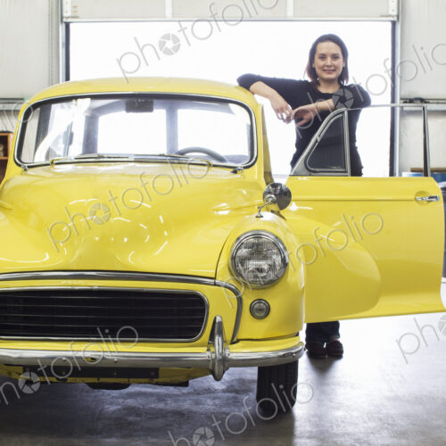 A caucasian female stands next to her old car in a classic car repair shop. A caucasian female stands next to her old car in a classic car repair shop.