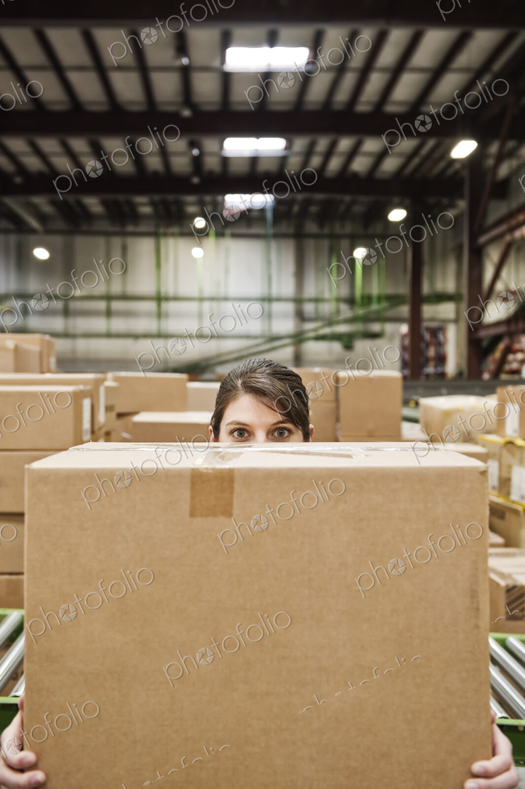 A caucasian female warehouse worker behind a cardboard box in a distribution warehouse.