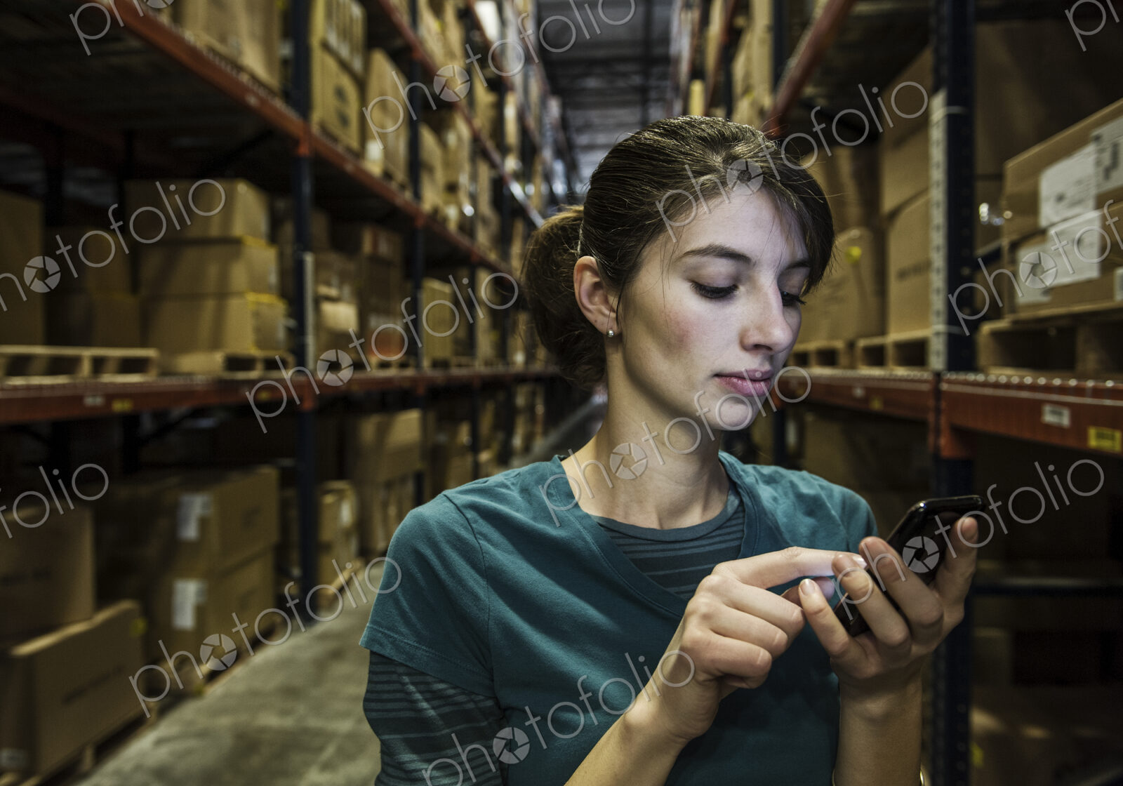 A caucasian female worker checking her phone for texts in warehouse