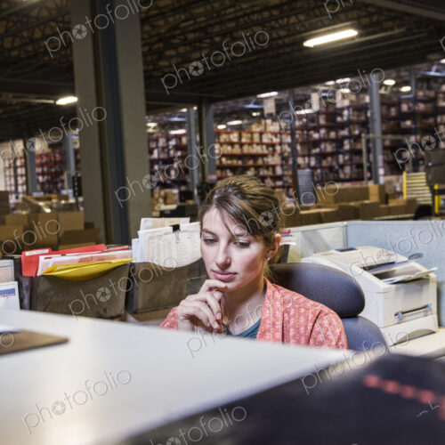 A caucasian female worker working on a computer problem in a distribution warehouse.