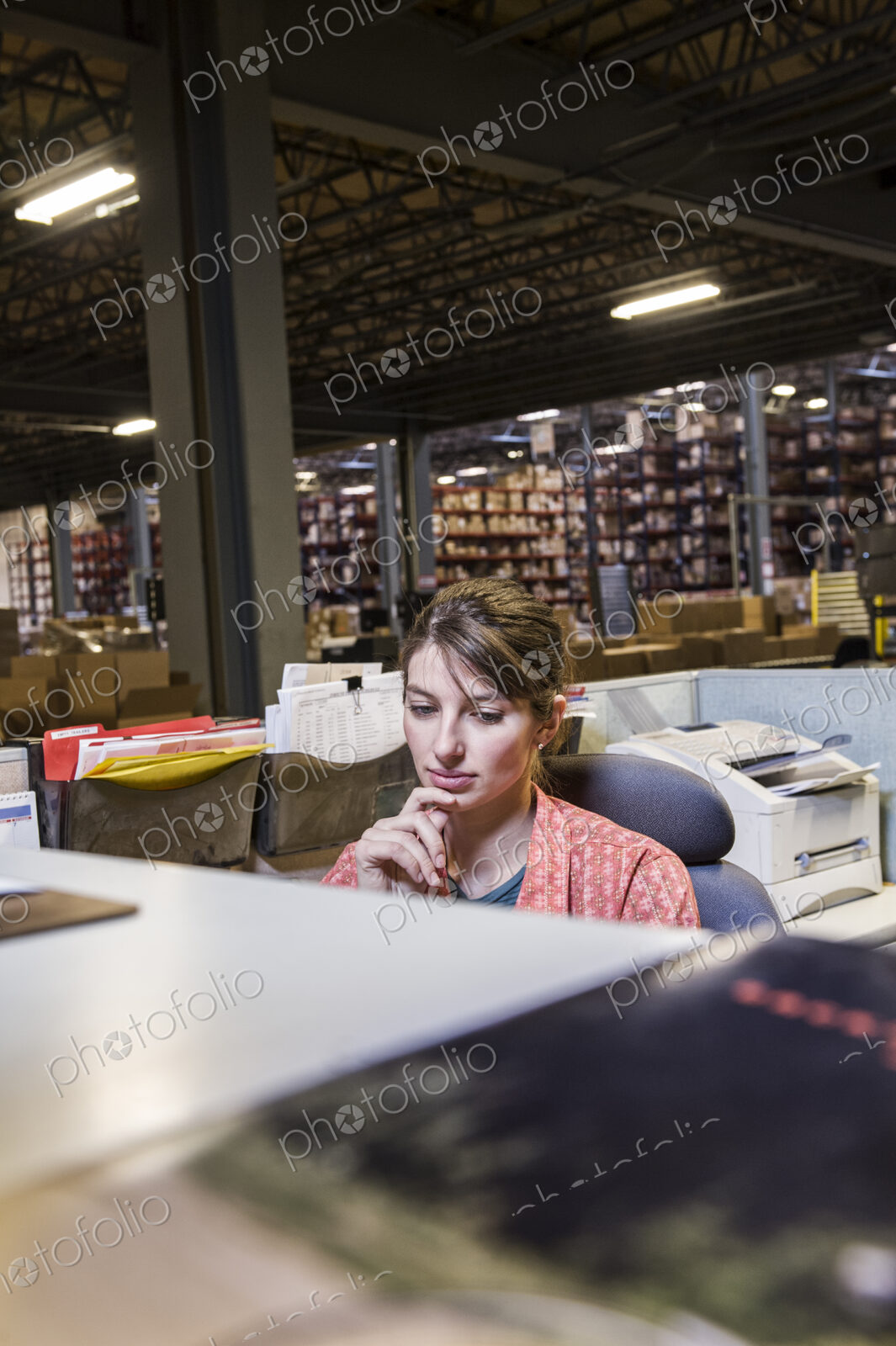 A caucasian female worker working on a computer problem in a distribution warehouse.