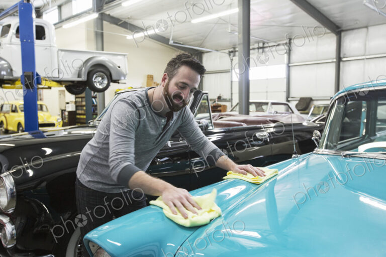 A caucasian male car mechanic applying wax to the hood of an old sedan in his classic…