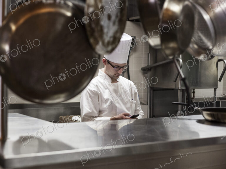 A caucasian male chef checking his cell phone in a commercial kitchen,