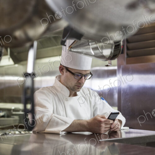 A caucasian male chef checking his cell phone in a commercial kitchen, A caucasian male chef checking his cell phone in a commercial kitchen,