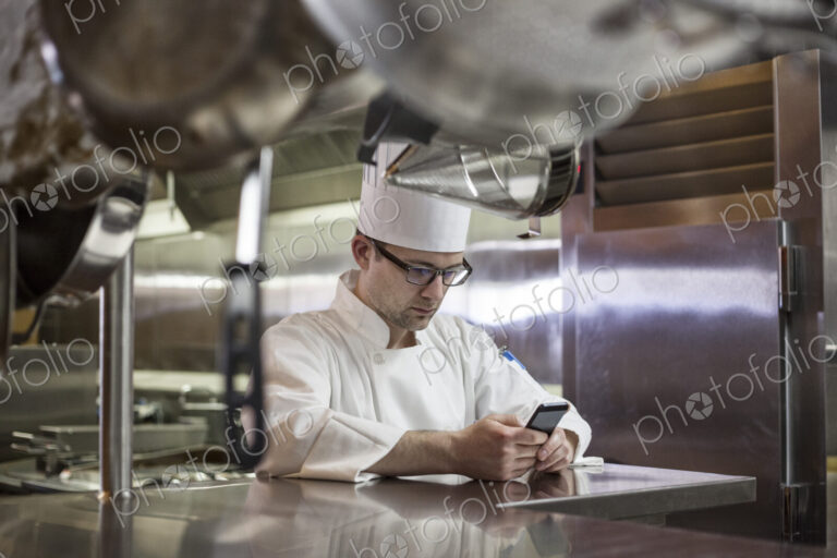 A caucasian male chef checking his cell phone in a commercial kitchen,