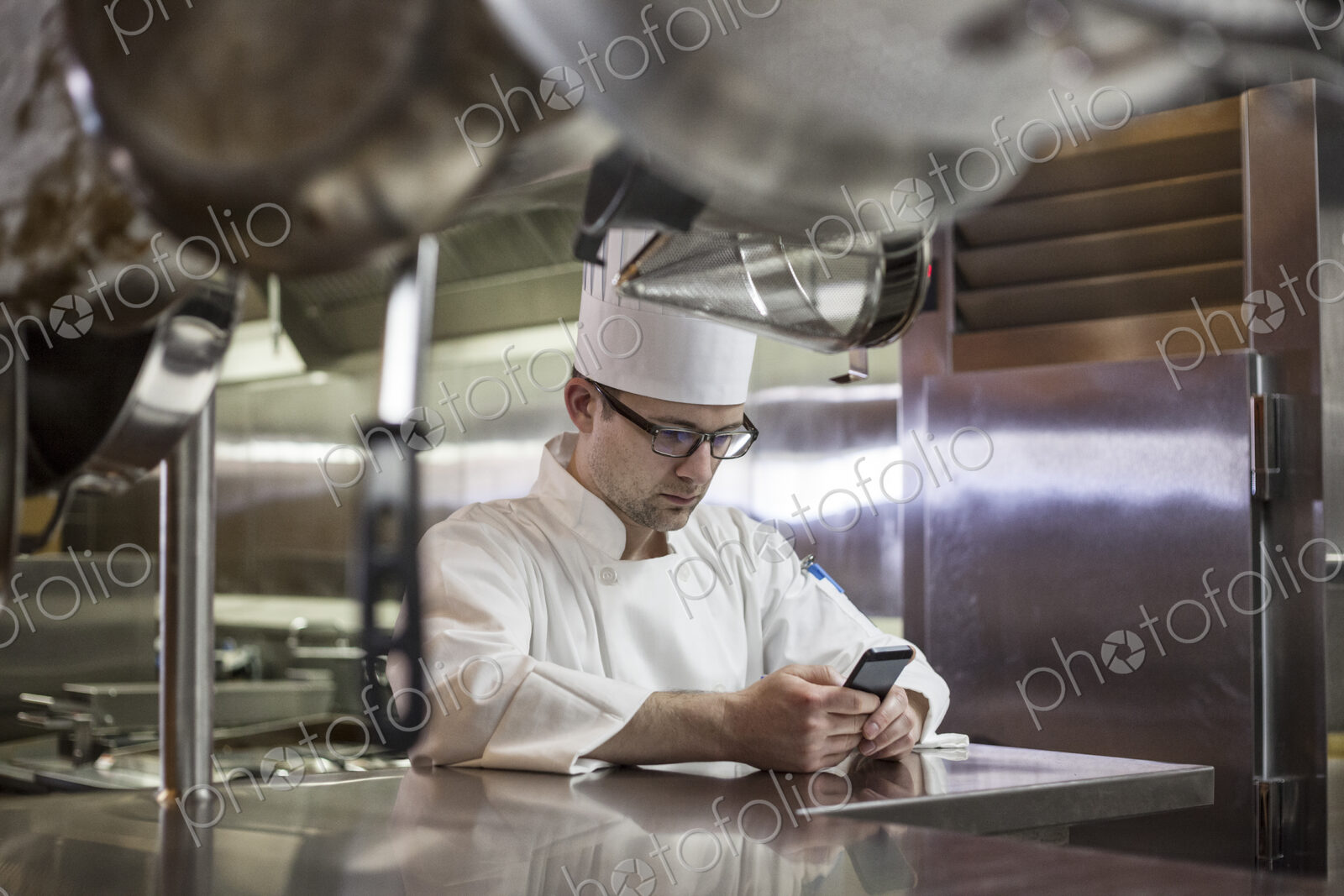 A caucasian male chef checking his cell phone in a commercial kitchen,