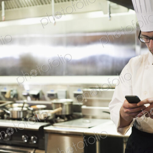 A caucasian male chef checking his cell phone in a commercial kitchen, A caucasian male chef checking his cell phone in a commercial kitchen,