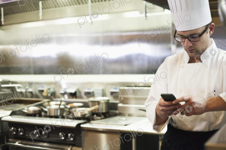 A caucasian male chef checking his cell phone in a commercial kitchen,