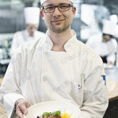 A caucasian male chef presenting a finished plate of fish in a commercial kitchen A caucasian male chef presenting a finished plate of fish in a commercial kitchen