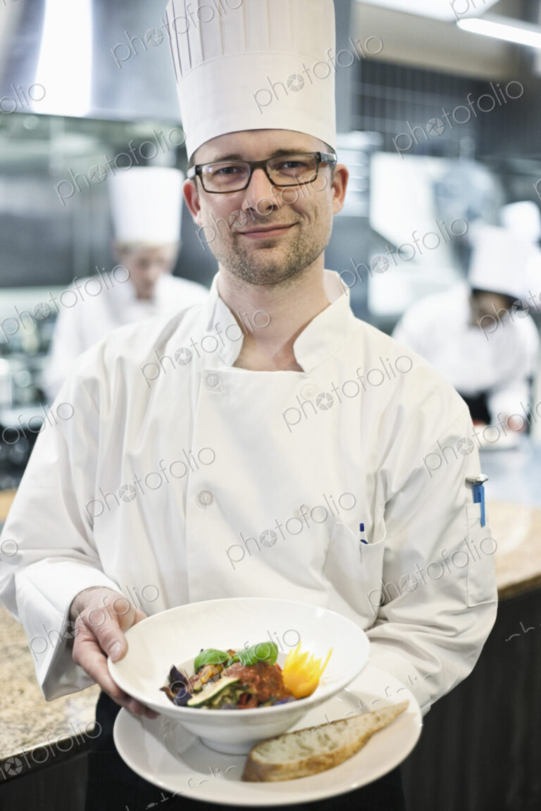 A caucasian male chef presenting a finished plate of fish in a commercial kitchen