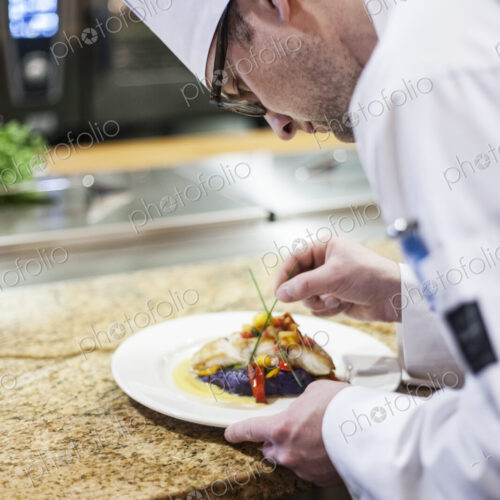 A caucasian male chef putting the finishing touches on a plate of fish in a commercial…