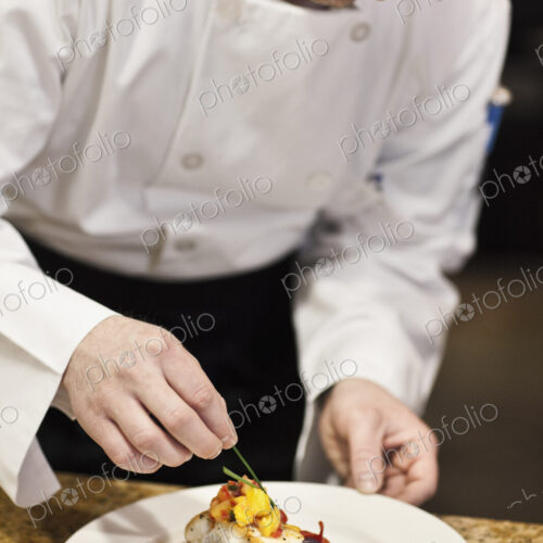 A caucasian male chef putting the finishing touches on a plate of fish in a commercial… A caucasian male chef putting the finishing touches on a plate of fish in a commercial…