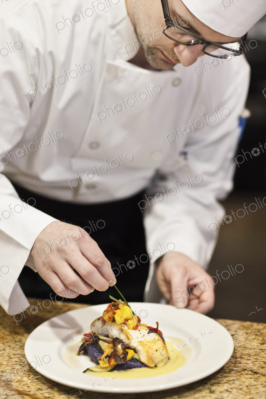 A caucasian male chef putting the finishing touches on a plate of fish in a commercial…