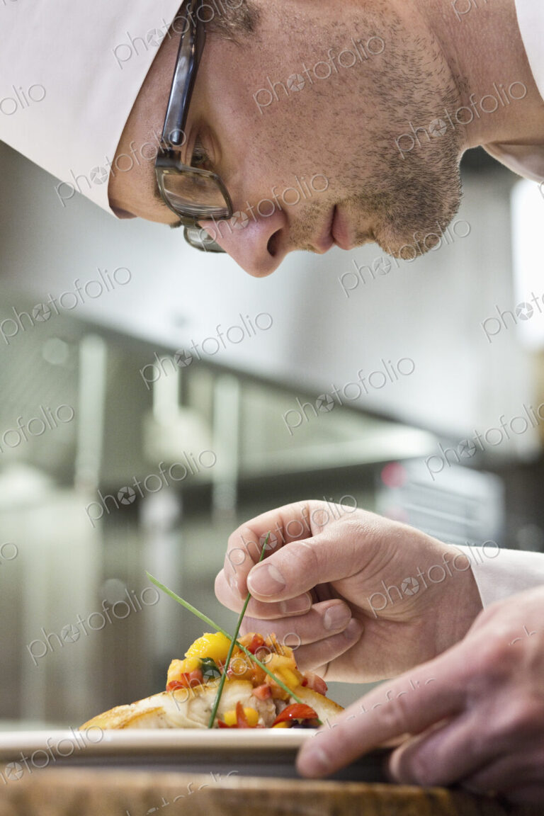 A caucasian male chef putting the finishing touches on a plate of fish in a commercial…