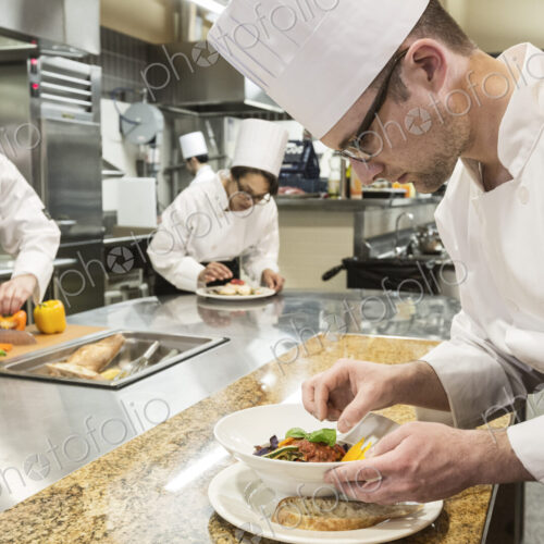 A caucasian male chef putting the finishing touches on a plate of fish in a commercial… A caucasian male chef putting the finishing touches on a plate of fish in a commercial…