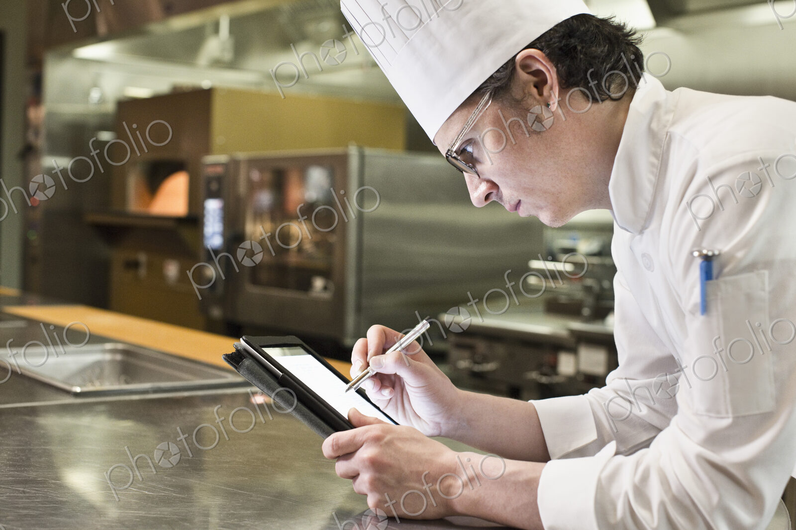 A caucasian male chef working on a notebook computer in a commercial kitchen.