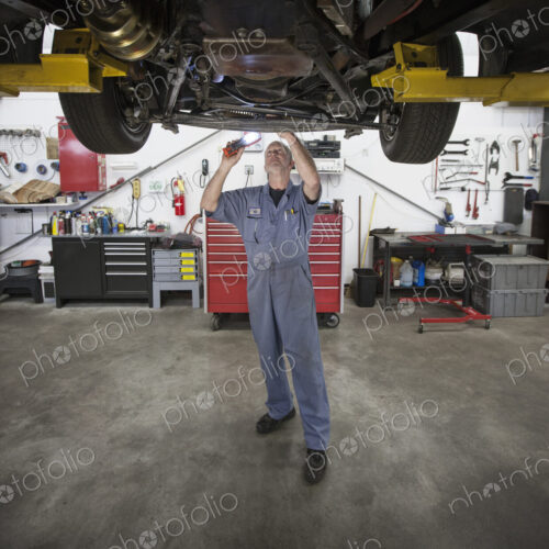 A caucasian male mechainc working on the underside of a car in the shop.