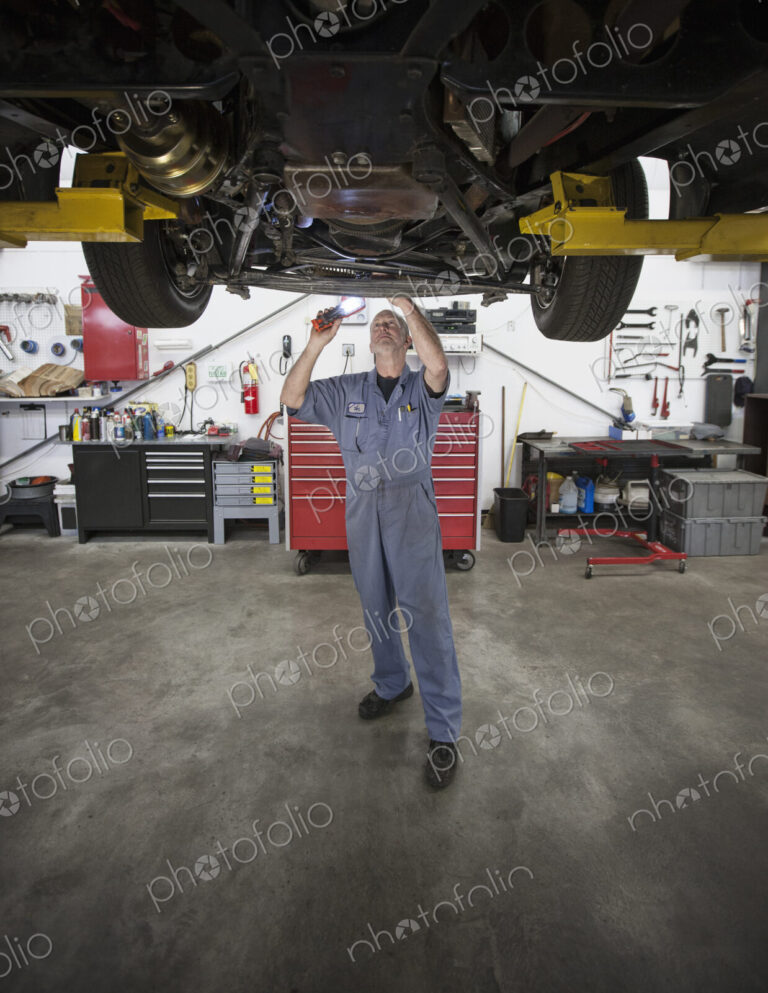 A caucasian male mechainc working on the underside of a car in the shop.