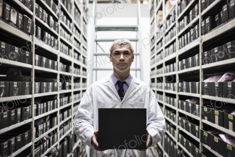 A caucasian male technician working on a laptop combuter among racks of machine parts
