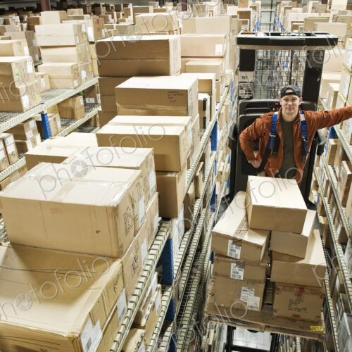 A caucasian male warehouse worker standing on a motorized stock picker and surrounded… A caucasian male warehouse worker standing on a motorized stock picker and surrounded…