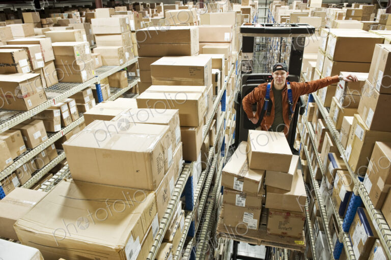 A caucasian male warehouse worker standing on a motorized stock picker and surrounded…