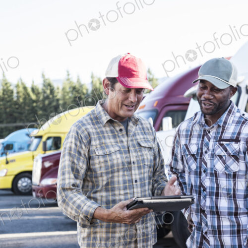A caucasian man and a black man truck driving team together in a truck stop parking lot. A caucasian man and a black man truck driving team together in a truck stop parking lot.