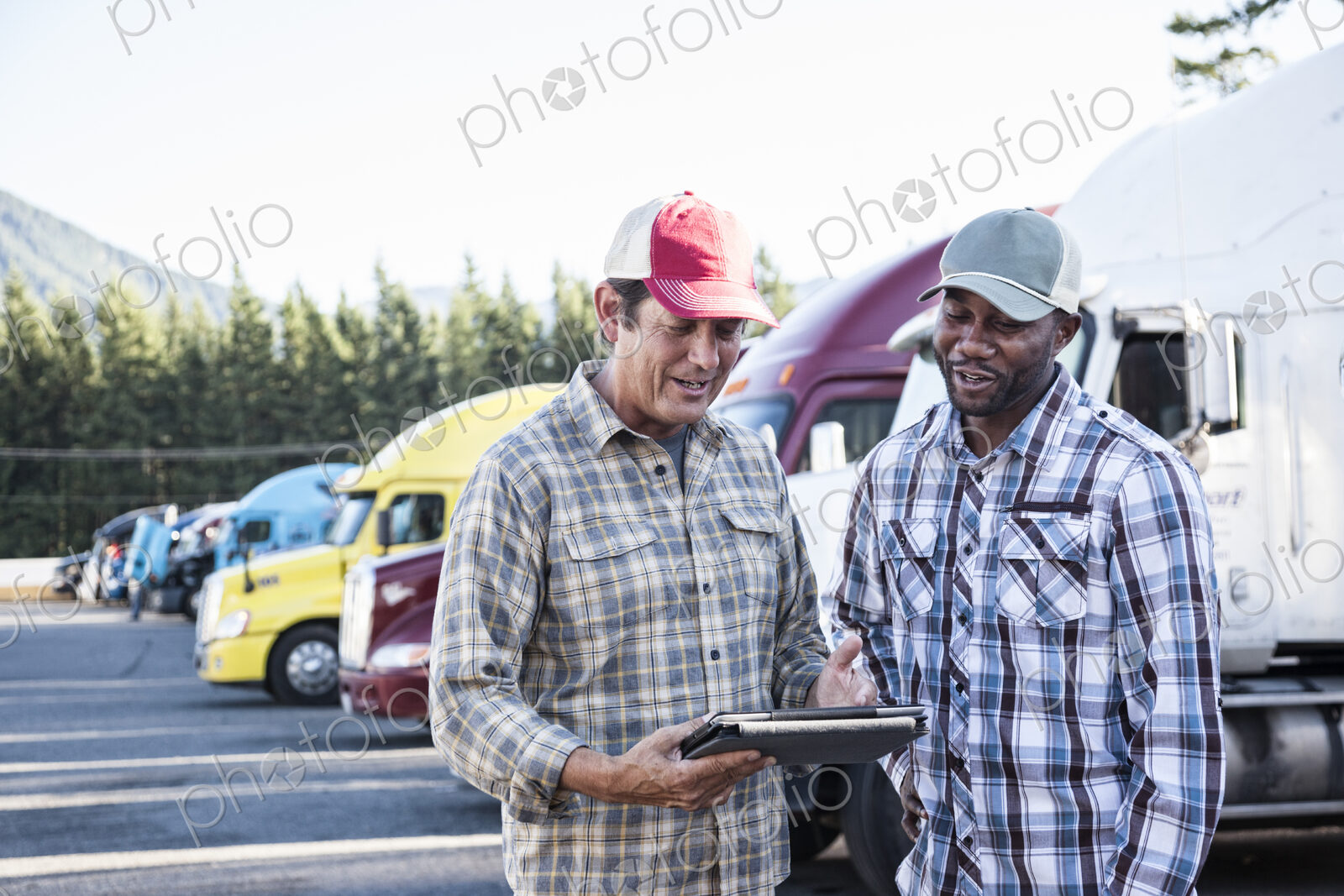 A caucasian man and a black man truck driving team together in a truck stop parking lot.