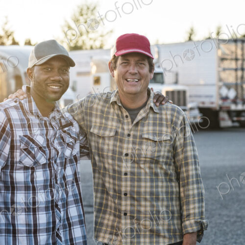 A caucasian man and a black man truck driving team together in a truck stop parking lot. A caucasian man and a black man truck driving team together in a truck stop parking lot.