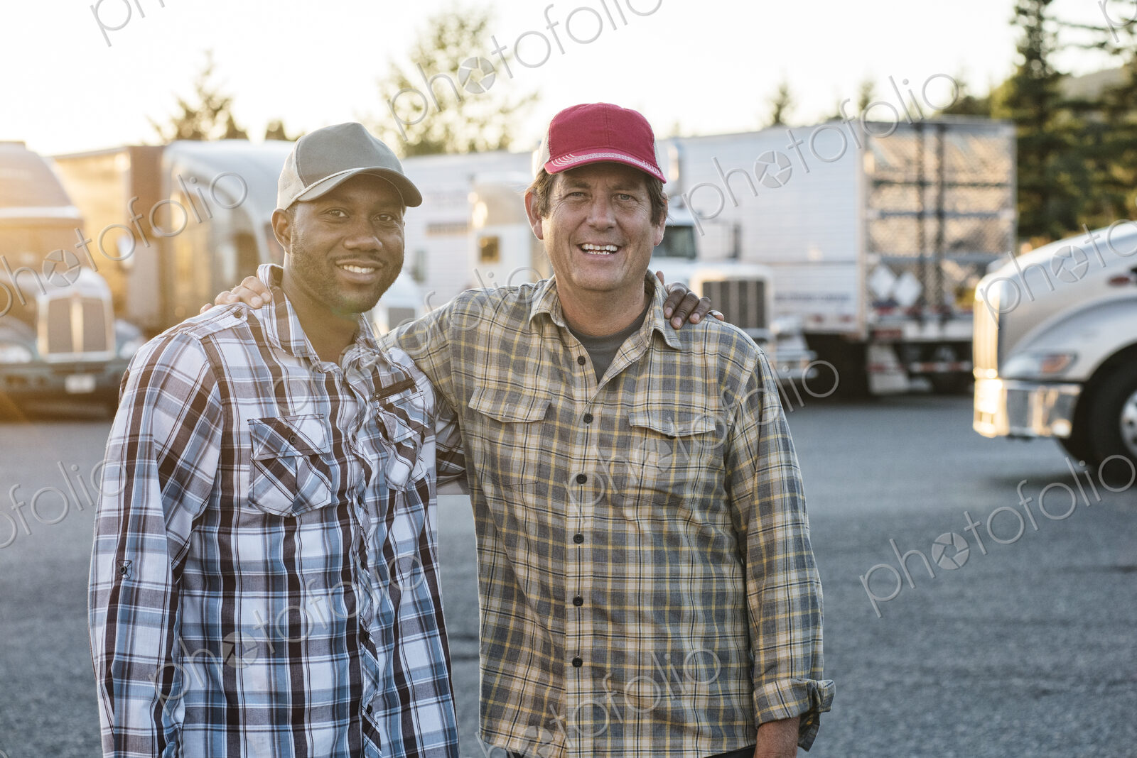 A caucasian man and a black man truck driving team together in a truck stop parking lot.