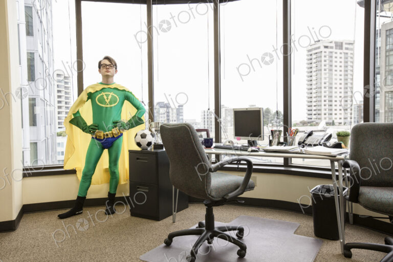 A caucasian man office super hero stands at his office window pondering his next move.