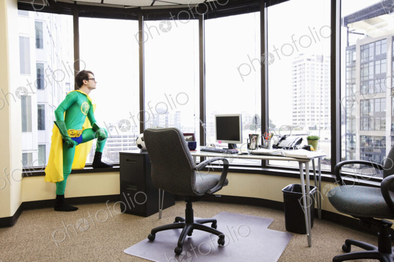 A caucasian man office super hero stands at his office window pondering his next…