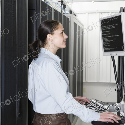 A caucasian woman computer technician working on servers in a computer server farm.