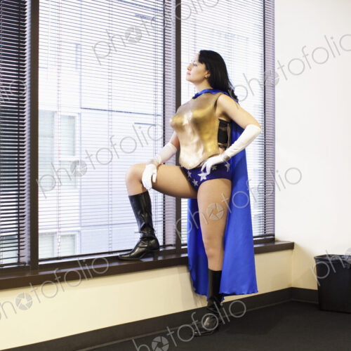 A caucasian woman office super hero stands at a window pondering her next move. A caucasian woman office super hero stands at a window pondering her next move.
