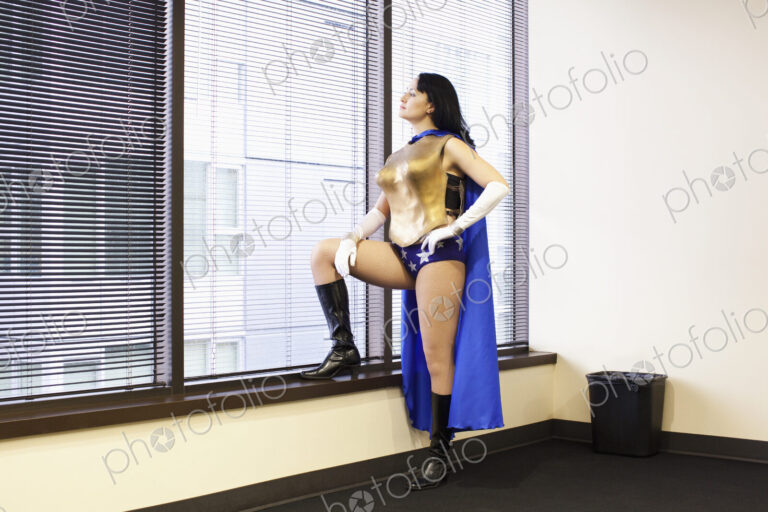 A caucasian woman office super hero stands at a window pondering her next move.