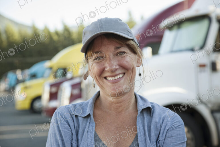 A caucasian woman truck driver near her truck parked in a parking lot of a truck stop.