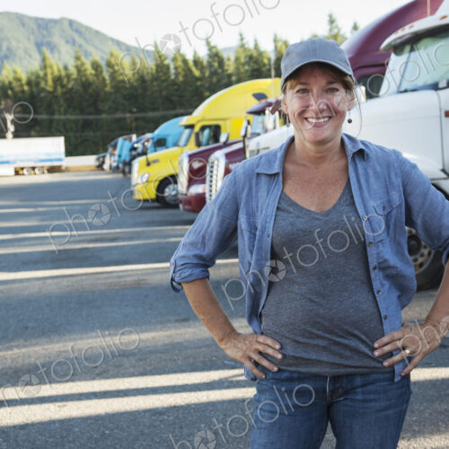 A caucasian woman truck driver near her truck parked in a parking lot of a truck stop.