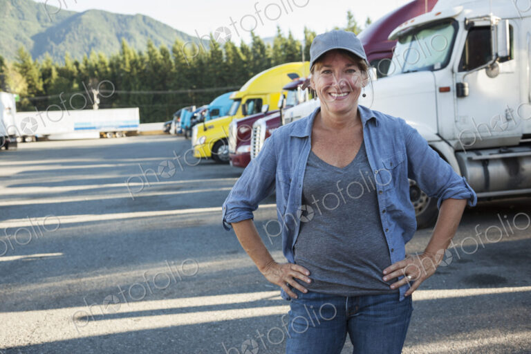 A caucasian woman truck driver near her truck parked in a parking lot of a truck stop.