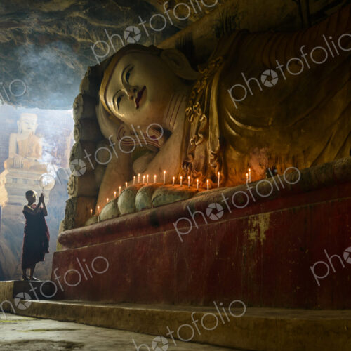 A cave temple, a large reclining Buddha statue, lit candles and a monk praying. A cave temple, a large reclining Buddha statue, lit candles and a monk praying.