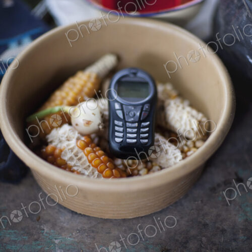 A cell phone,mobile communications,a handset or telephone,in a bowl of maize kernels.