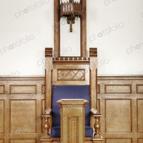 A ceremonial chair in a large auditorium in a historic building with a blue seat and…