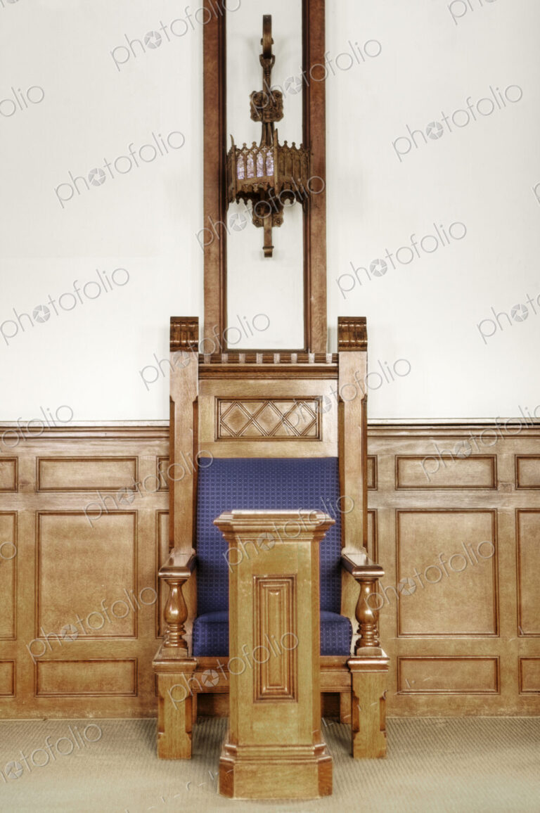 A ceremonial chair in a large auditorium in a historic building with a blue seat and…