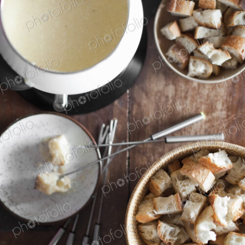 A cheese fondue on a table top. Cubed bread and long forks, for dipping bread into… A cheese fondue on a table top. Cubed bread and long forks, for dipping bread into…