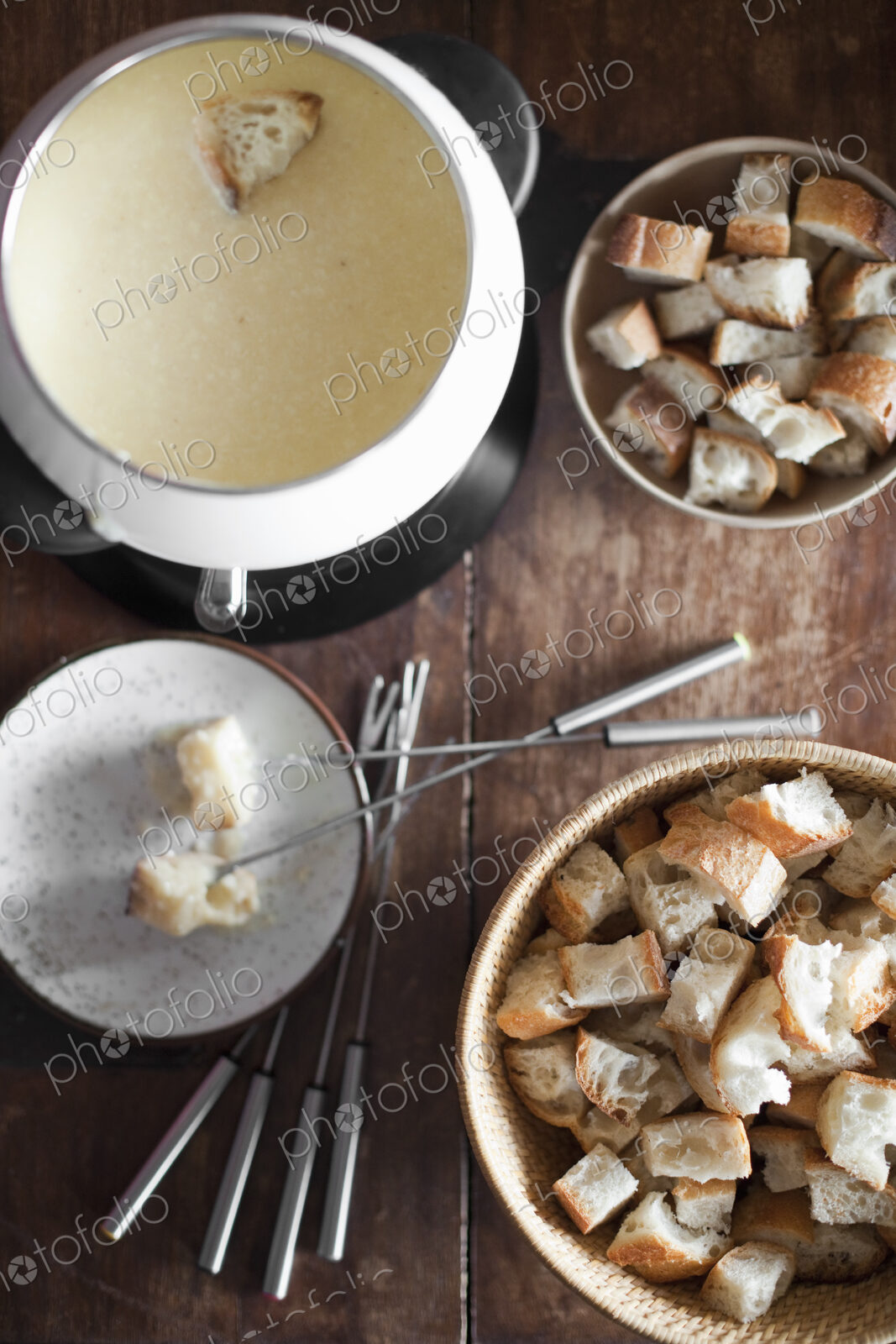 A cheese fondue on a table top. Cubed bread and long forks, for dipping bread into…